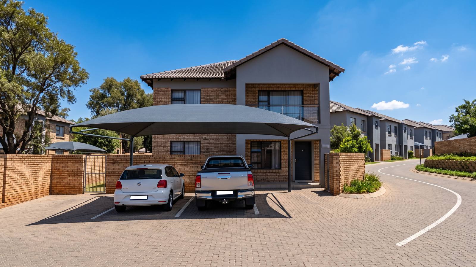 Charcoal double shade net carport in front of a grey two-storey townhouse in a complex.